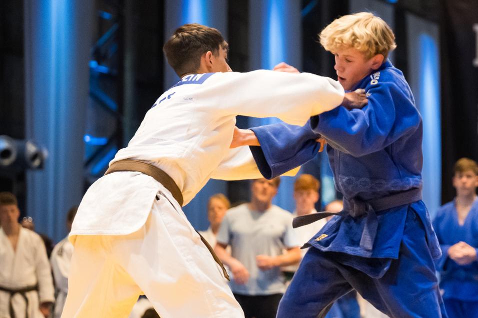Zwei Jugendliche im Judoanzug kämpfen auf einer gelben Matte bei den Ruhr Games, während Zuschauer im Hintergrund beobachten.
